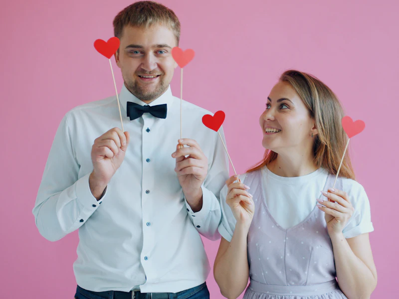 Couple posing with heart props against a pink backdrop
