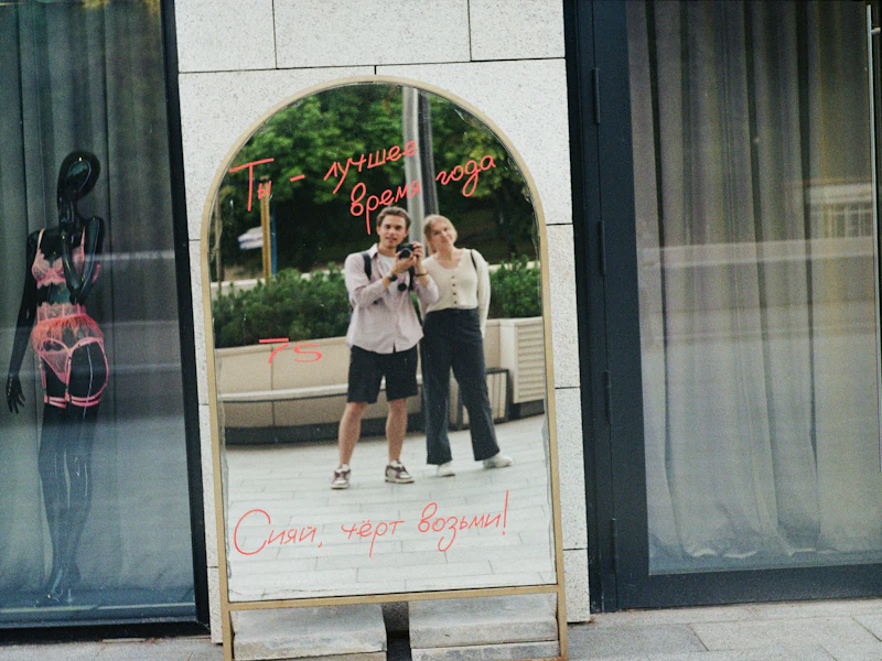 Two people taking a photo in a tall arched mirror with lettering on the glass